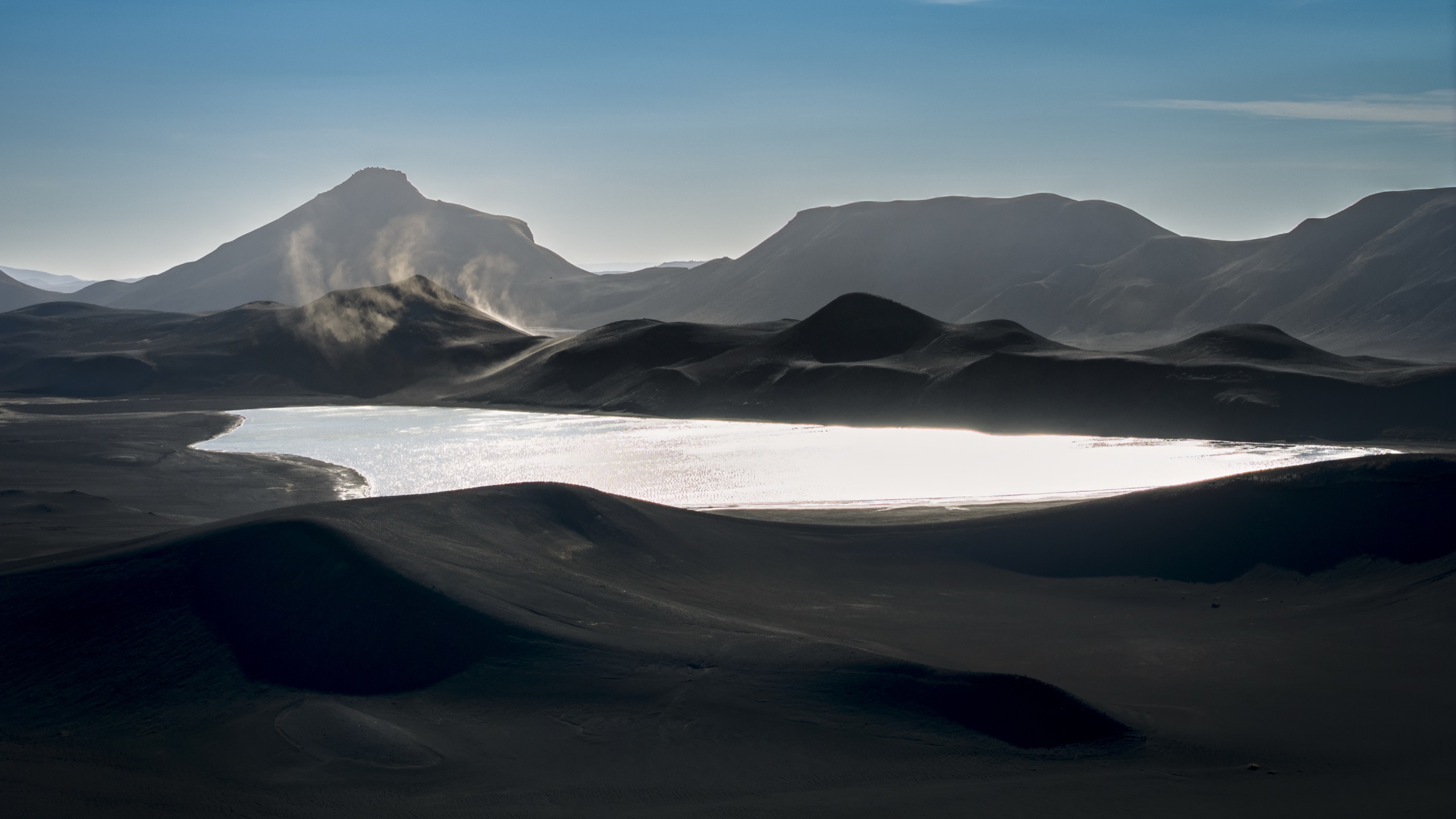 Backlit volcanic dunes and a silver highland lake